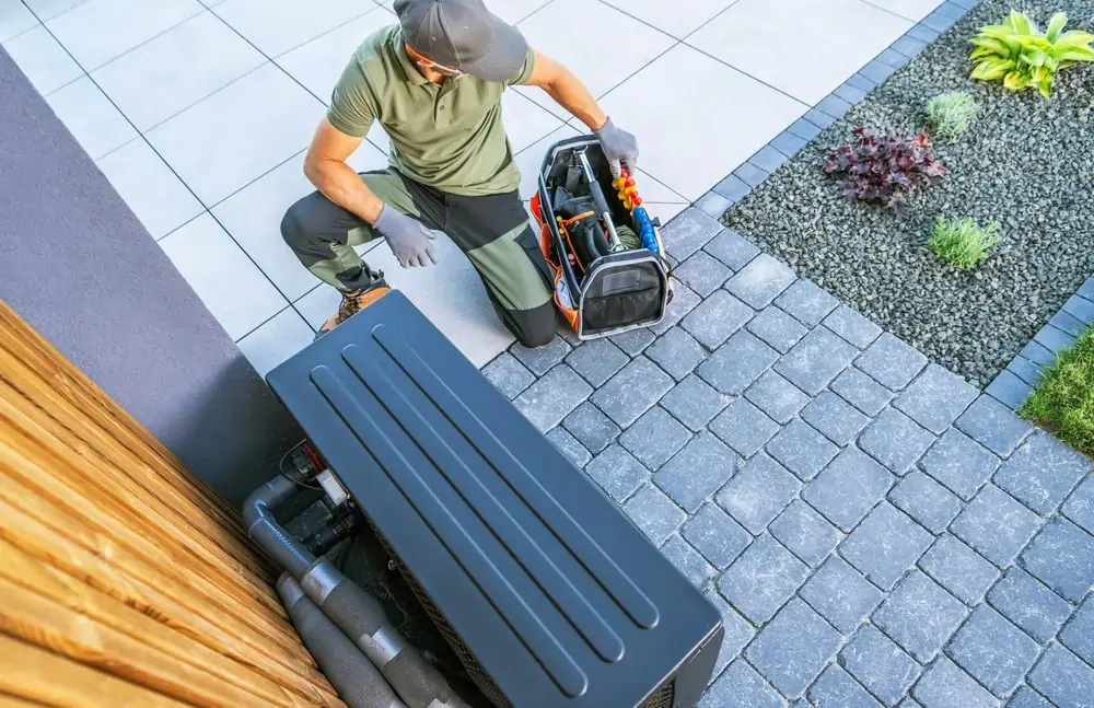 Technik inštaluje vonkajšiu jednotku tepelného čerpadla na dlažbe vedľa záhrady s kvetmi